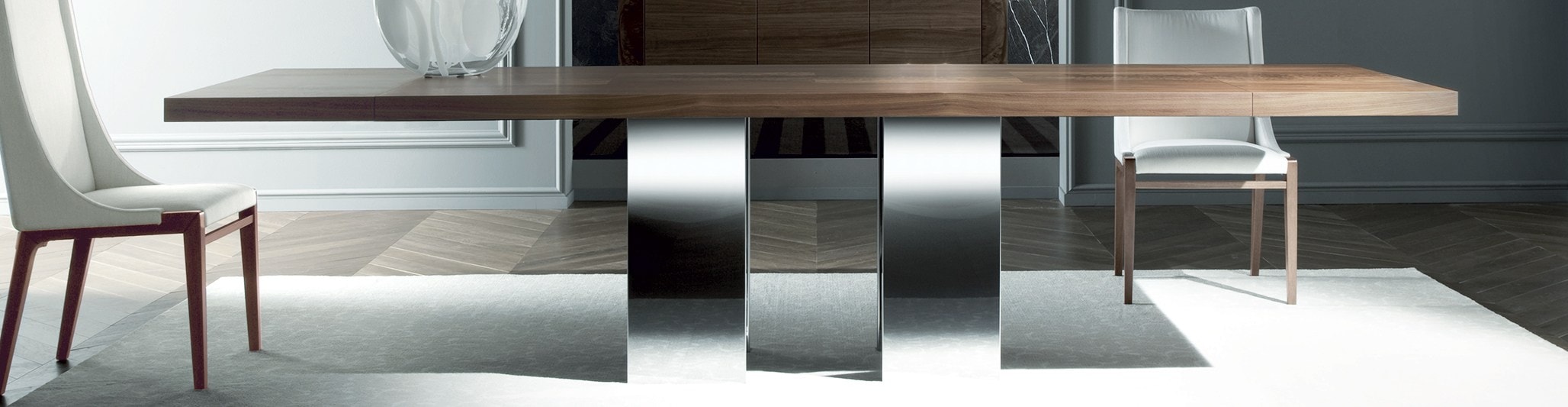 Rectangular wooden dining table with polished metal base and two upholstered chairs in a dining room setting