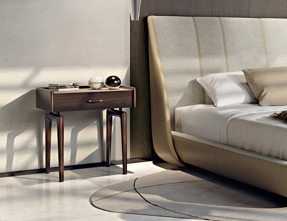 Wood bedside table in walnut finish beside upholstered bed